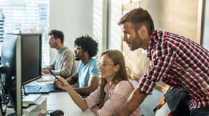 Une équipe de jeunes développeurs assis chacun sur leur bureau, collaborant tout en travaillant sur des ordinateurs. Des codes informatiques sont affichés sur les écrans. Ambiance créative et professionnelle dans un bureau moderne.